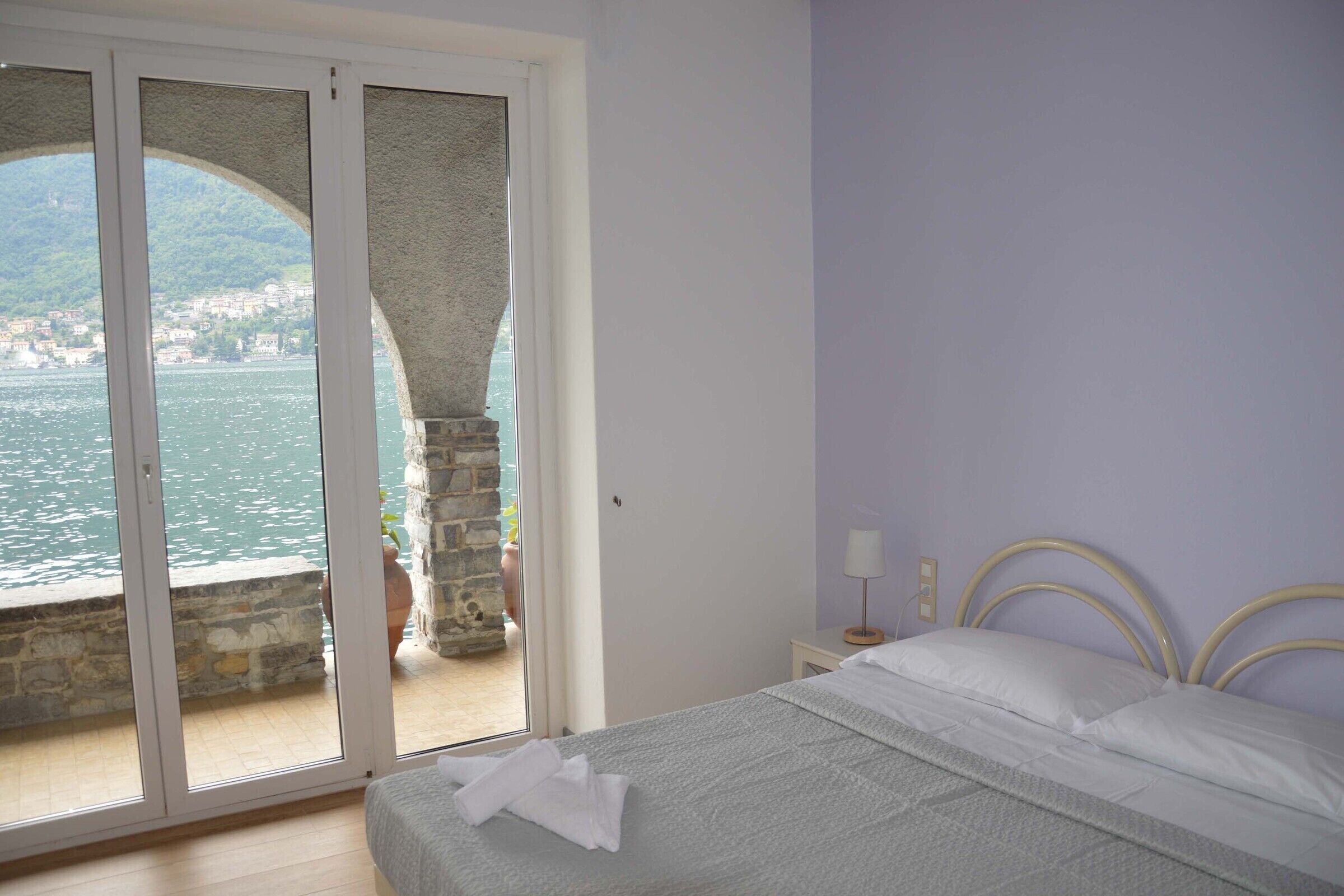 Un dormitorio con una cama, una mesita de noche y vistas a un cuerpo de agua y un pueblo a través de una puerta de vidrio.