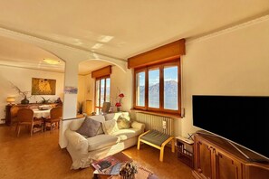 A living room with a sofa, a coffee table, a TV, and a view of mountains through large windows.