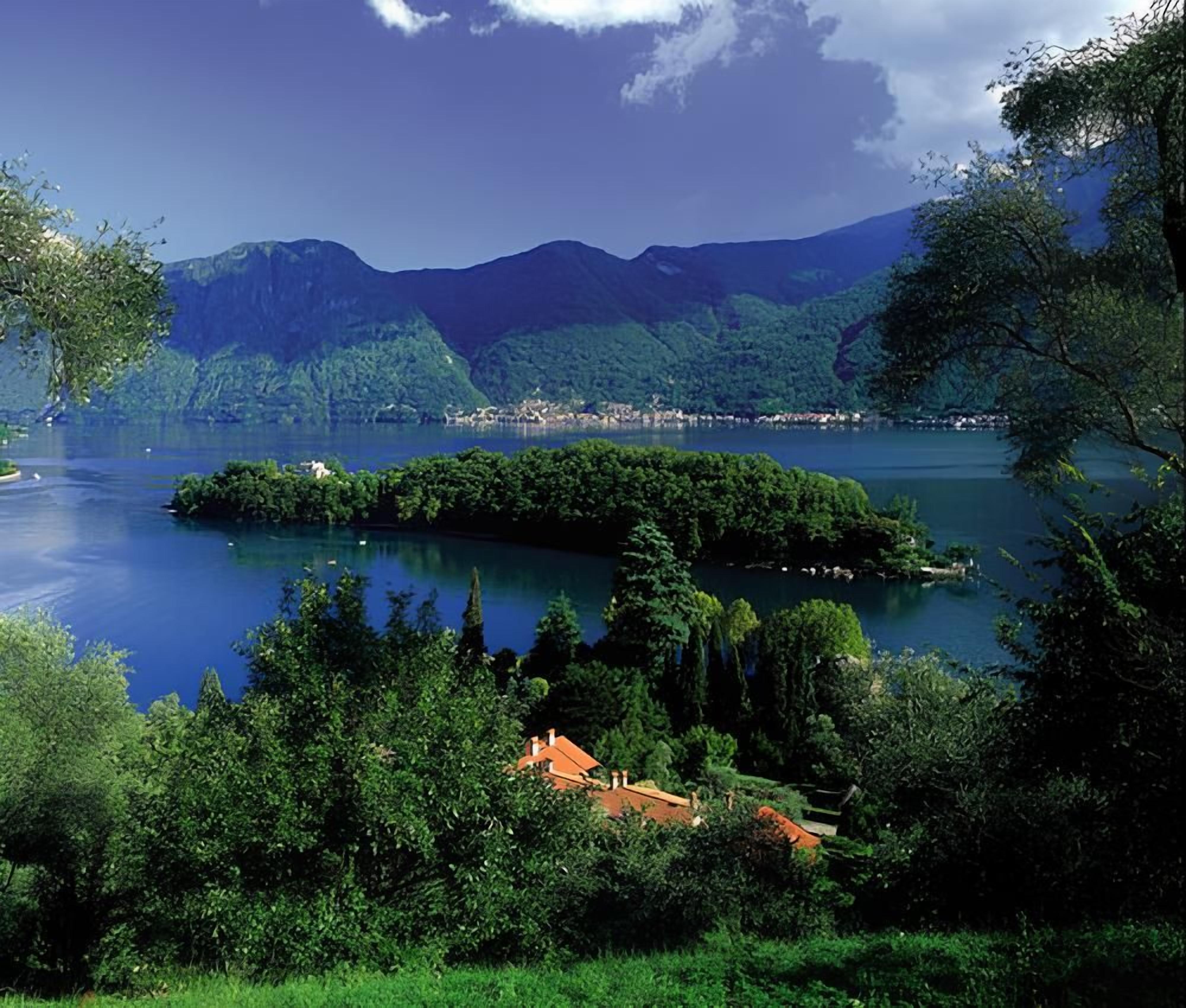 Un lac entouré d’une végétation luxuriante et de montagnes, avec une petite île et un bâtiment au premier plan.