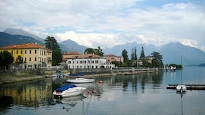 Un pueblo a orillas del lago con edificios históricos, barcos amarrados en la costa y montañas al fondo.