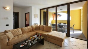 Un salón con un sofá seccional color beige, una mesa de centro con objetos decorativos y un ventanal corredizo que da a un comedor.