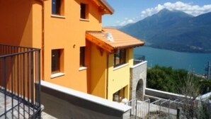 Un edificio de dos pisos con fachada amarilla y un balcón, con vista a un lago y montañas.