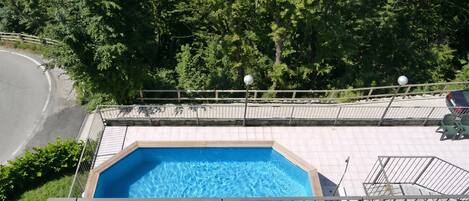 A swimming pool with a tiled deck, surrounded by a metal fence and trees.