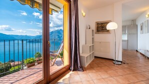 A balcony with a view of the sea and mountains, a chair, a floor lamp, and a white shelving unit. - Alto Perledo Terrazzo (Perledo)