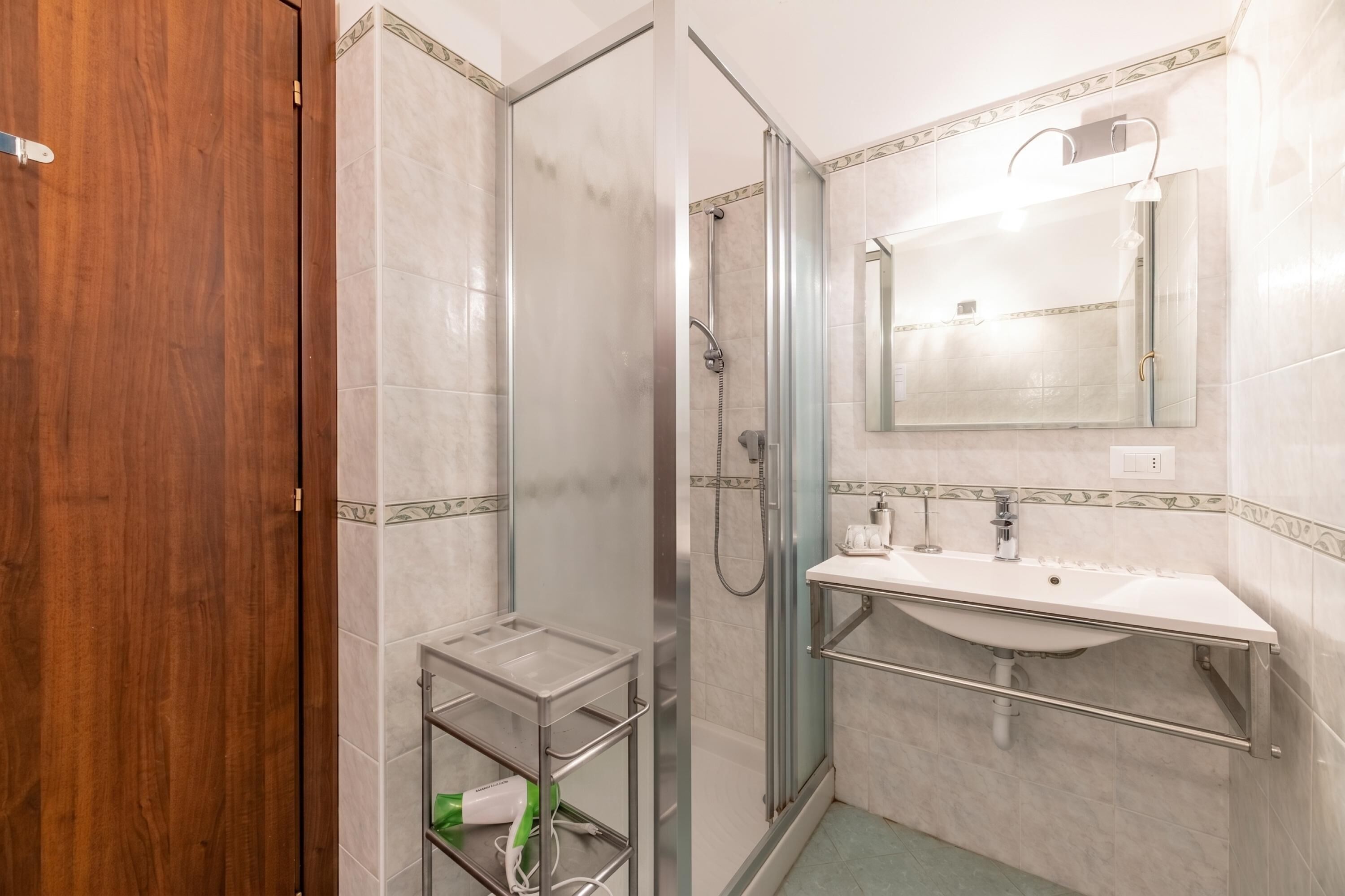 Un baño con ducha, lavamanos, espejo y puerta de madera.