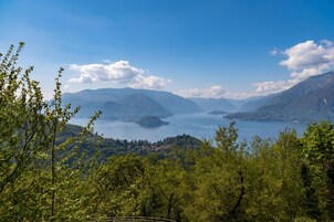 Paisagem montanhosa com um lago, árvores e edifícios ao longe.