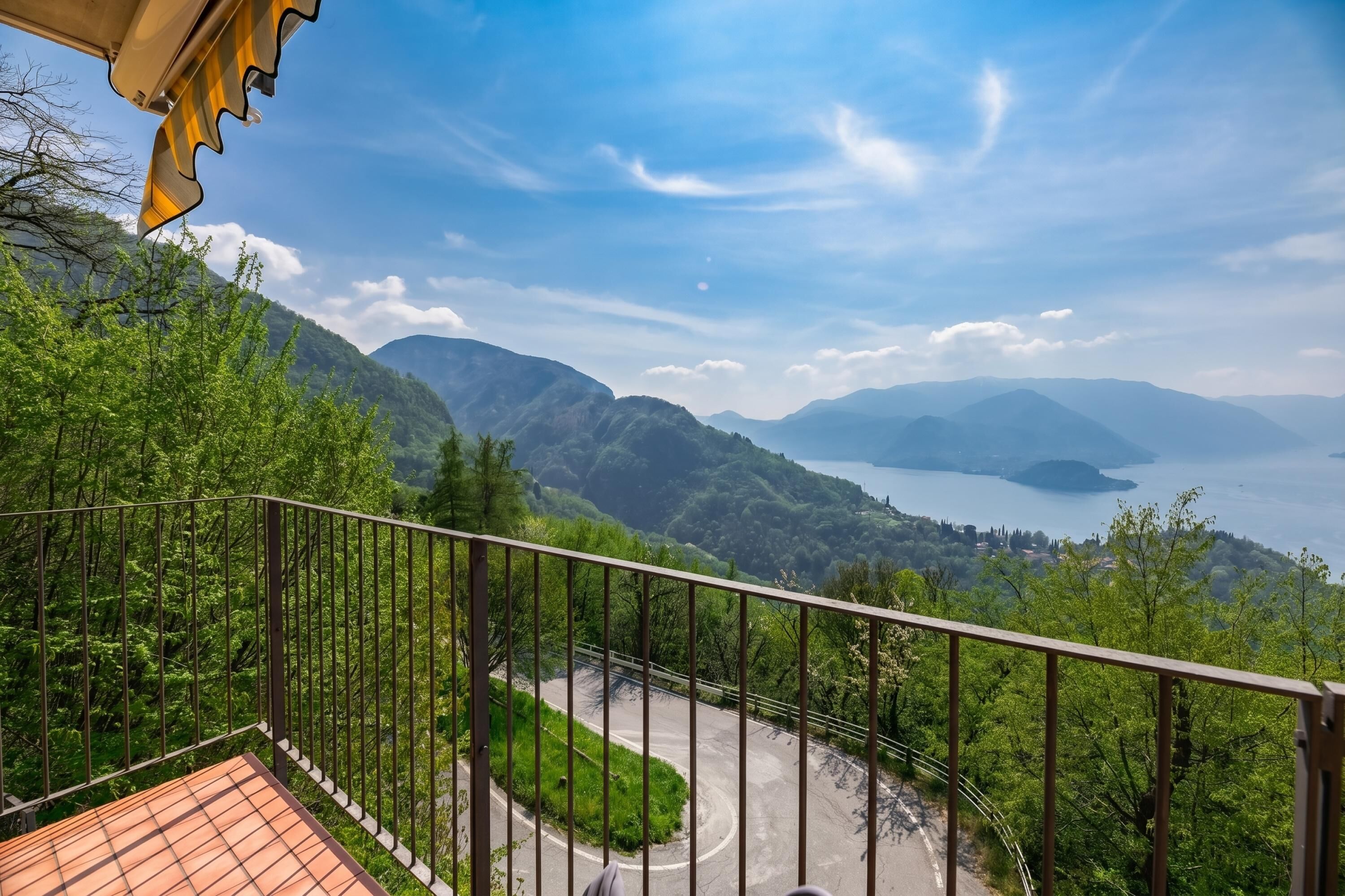 Ein Balkon mit Blick auf eine kurvenreiche Straße, üppiges Grün und entfernte Berge.