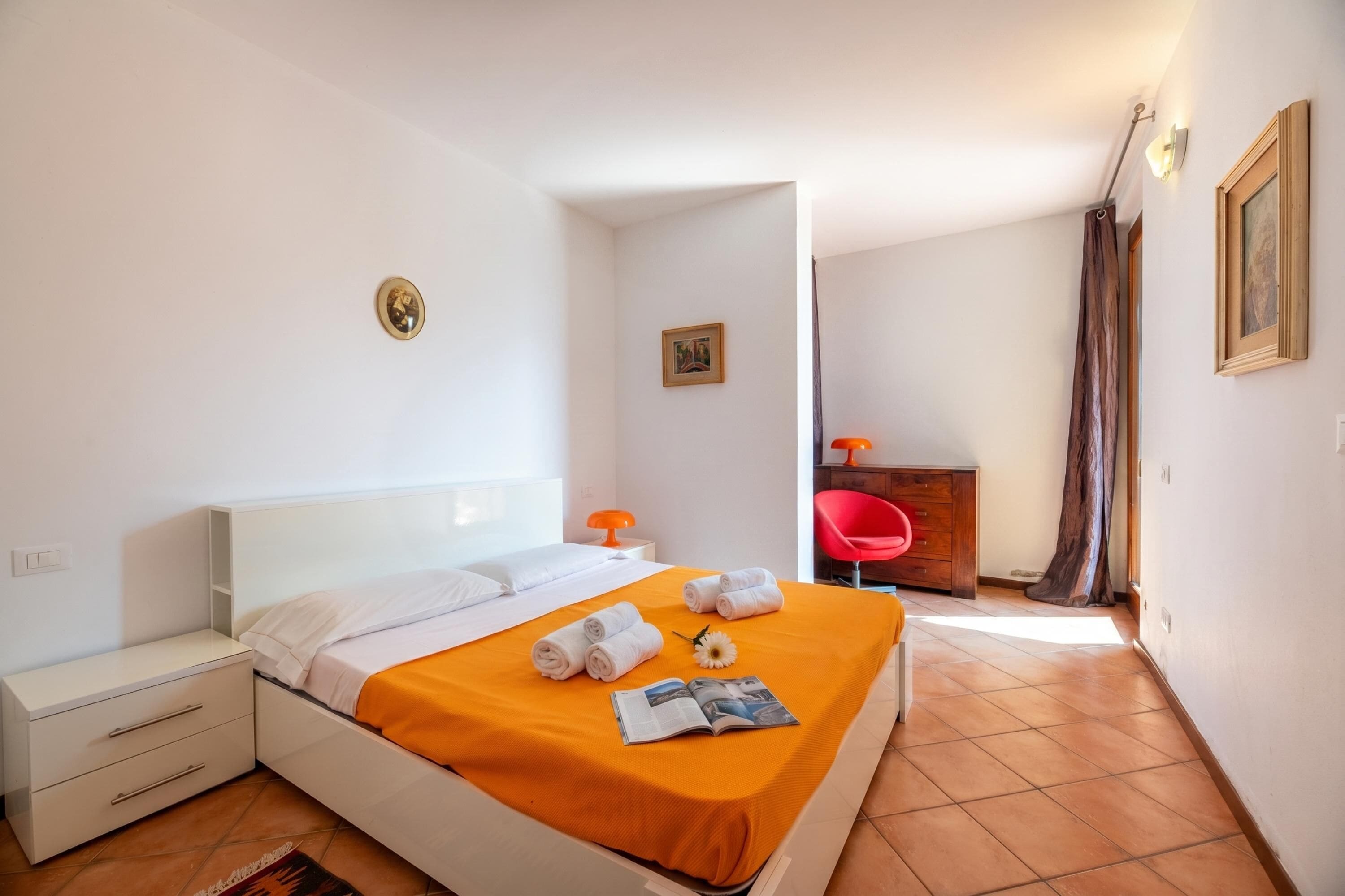 A neatly made bed with a white headboard, a small bedside table, and a red chair in the corner.