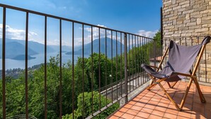 A balcony with a view of mountains and a lake, a brick wall, and a folding chair. - Alto Perledo Terrazzo (Perledo)