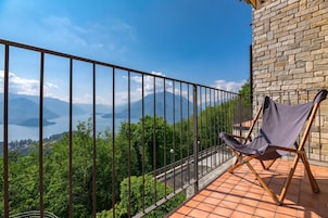 Un balcon avec vue sur les montagnes et un lac, un mur en briques et une chaise pliante.