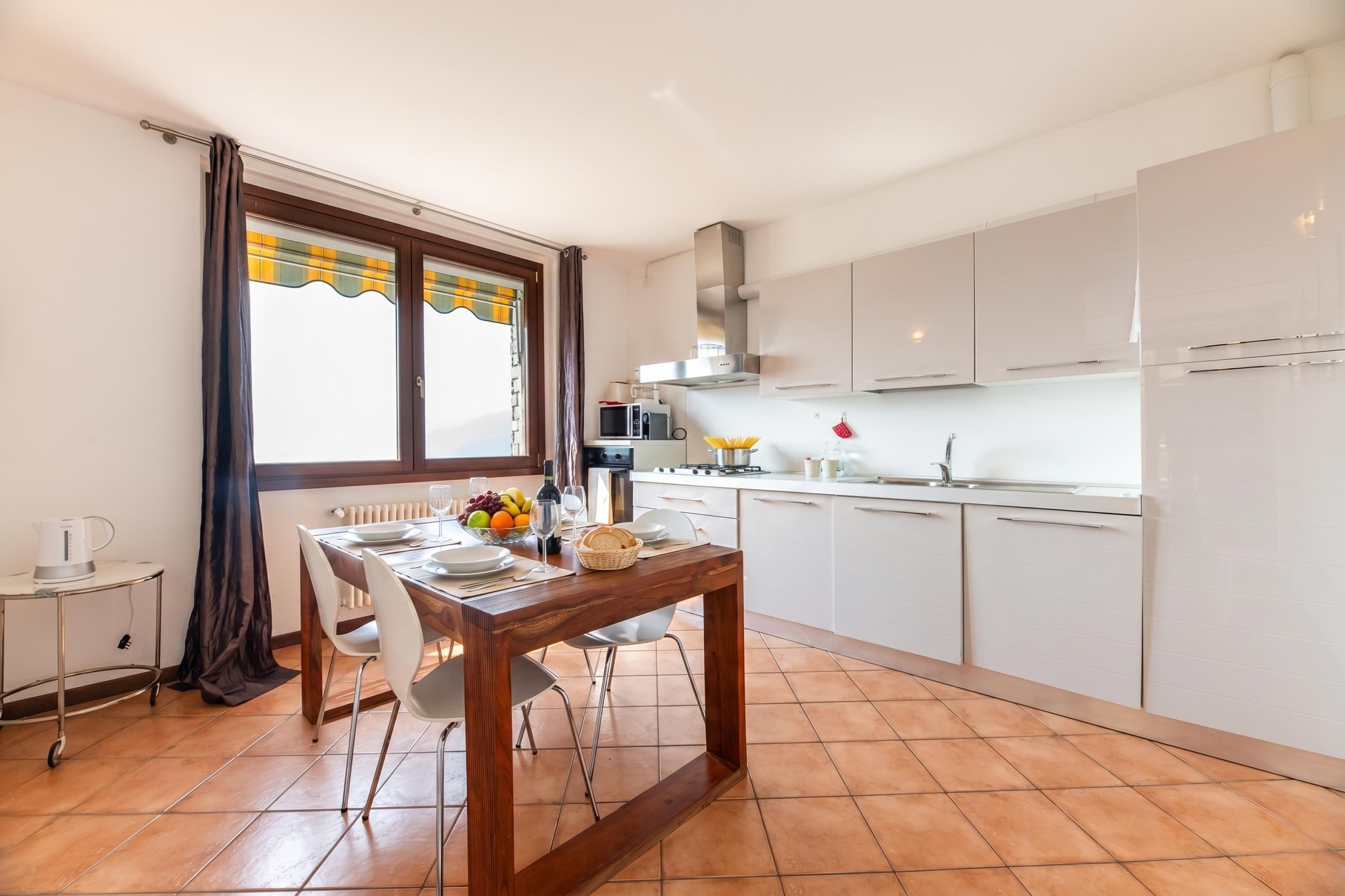 A modern kitchen with white cabinets, a dining table with chairs, and a window with curtains.