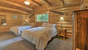 A log cabin bedroom with two beds, a window, and a wooden cabinet.