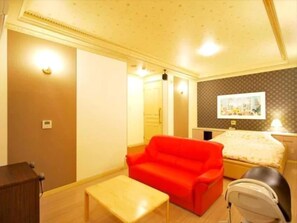 A hotel room with a bed, a red sofa, a small table, and a wheelchair. - Hotel Com - Adults Only (Nagoya)