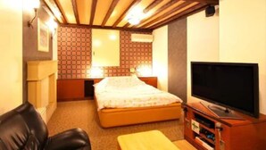 Ein Hotelzimmer mit einem Bett, einem Fernseher, einer hölzernen Bank und einem kleinen Tisch.