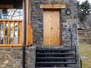 A stone building with a wooden door, a window with a wooden frame, and a black staircase leading to the entrance.