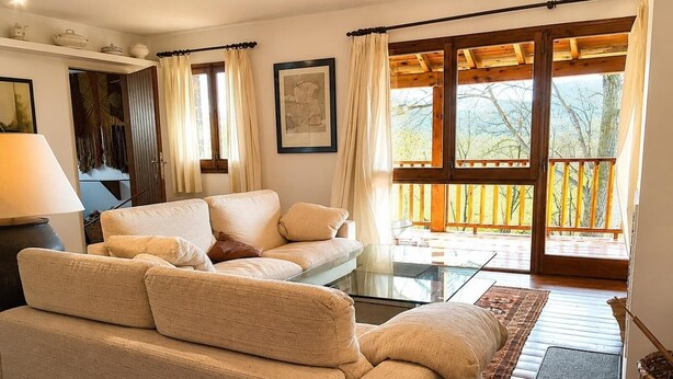 A living room with a sofa, a glass coffee table, a lamp, a framed picture, and a view of a balcony with wooden railings. - Duplex 3 Bed Rustic Style, Fireplace, Terrace & Cadí Views (Guils de Cerdanya)