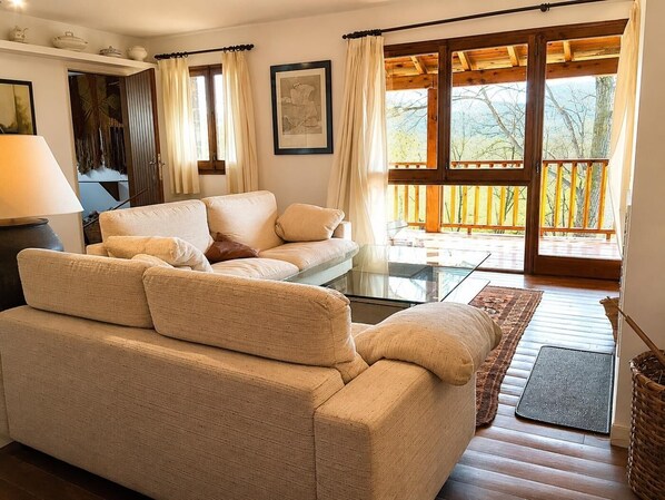 A living room with a sofa, a glass coffee table, a lamp, a framed picture, and a view of a balcony with wooden railings.