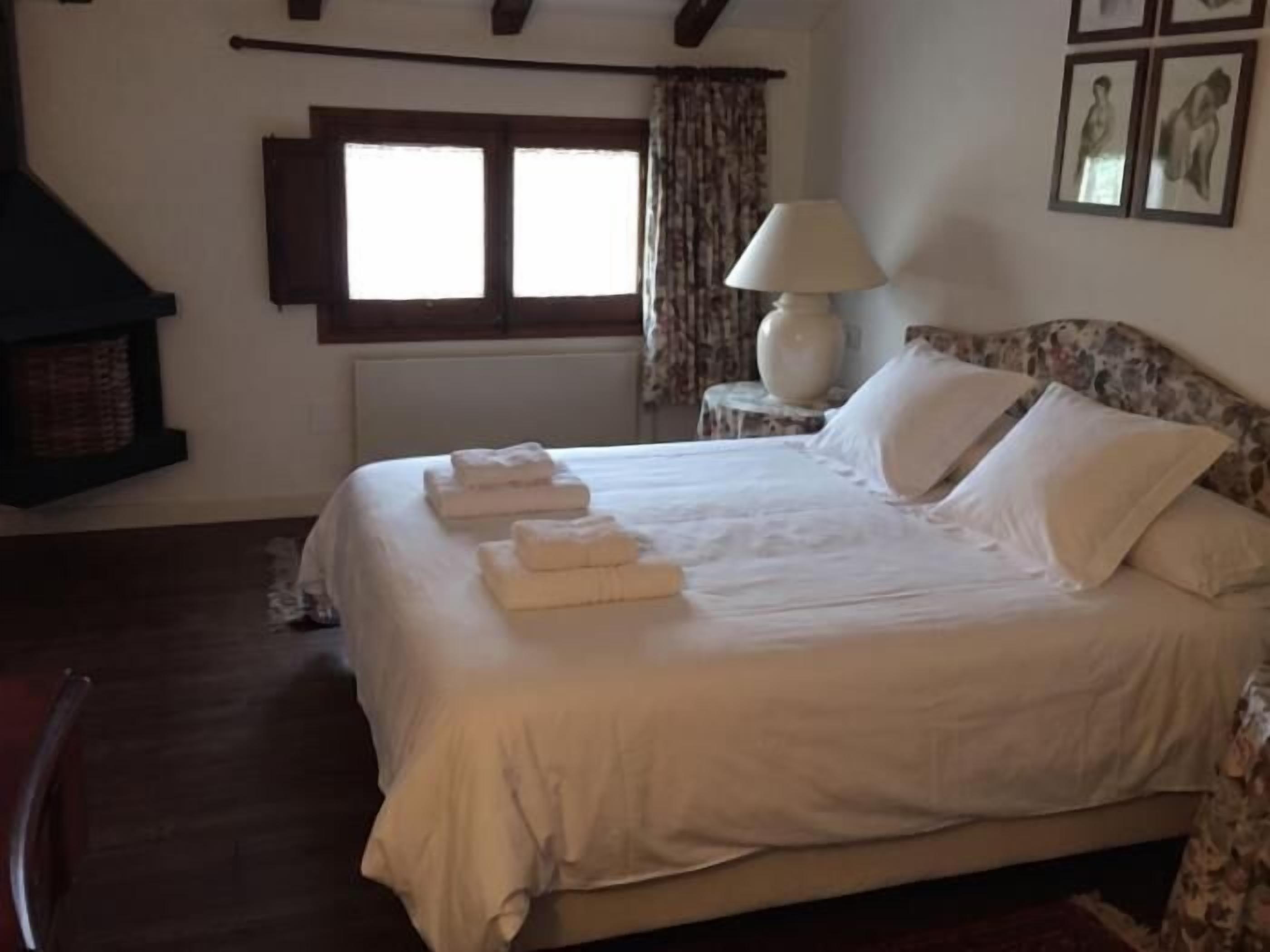 Un dormitorio con cama, mesita de noche, lámpara y ventana.