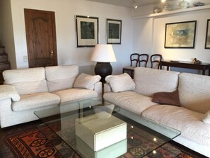 A living room with two sofas, a glass coffee table, a lamp, framed pictures on the wall, and a patterned rug.
