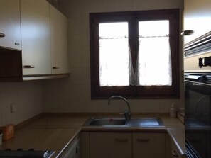 Una cocina con ventana, pileta, alacenas y estufa.
