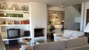 A living room with a sofa, a fireplace, a television, and shelves with books and decorative items. - Duplex 3 Bed Rustic Style, Fireplace, Terrace & Cadí Views (Guils de Cerdanya)