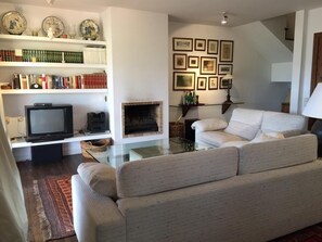 A living room with a sofa, a fireplace, a television, and shelves with books and decorative items.