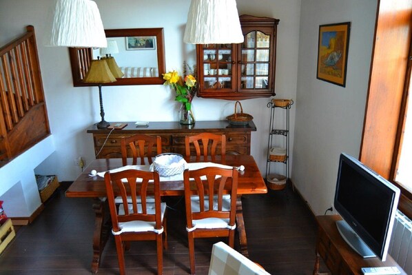 Un coin repas comprenant une table en bois, des chaises, un vase avec des fleurs, un meuble et un téléviseur.
