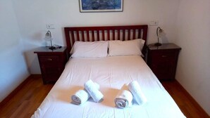 A neatly made bed with white linens and rolled towels, two bedside tables with lamps, and a painting on the wall. - House 3 rooms Fireplace, Garden & Dryer (Guils de Cerdanya)