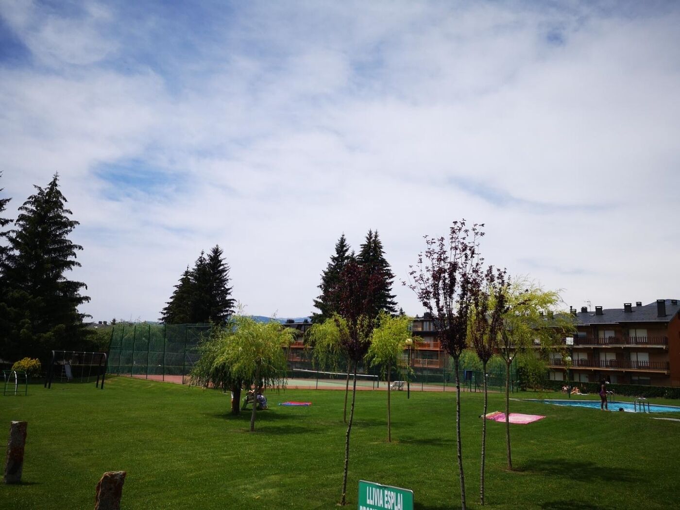 A grassy area with a sign reading 'LLIVIA ESPAI', trees, and a building in the background.
