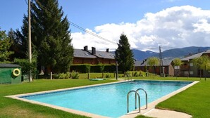 Une piscine rectangulaire avec des échelles en métal, entourée d’une pelouse bien entretenue, d’arbres et avec une chaîne de montagnes en toile de fond.