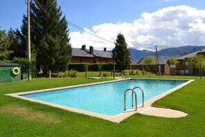 Une piscine rectangulaire avec des échelles en métal, entourée d’une pelouse bien entretenue, d’arbres et avec une chaîne de montagnes en toile de fond.