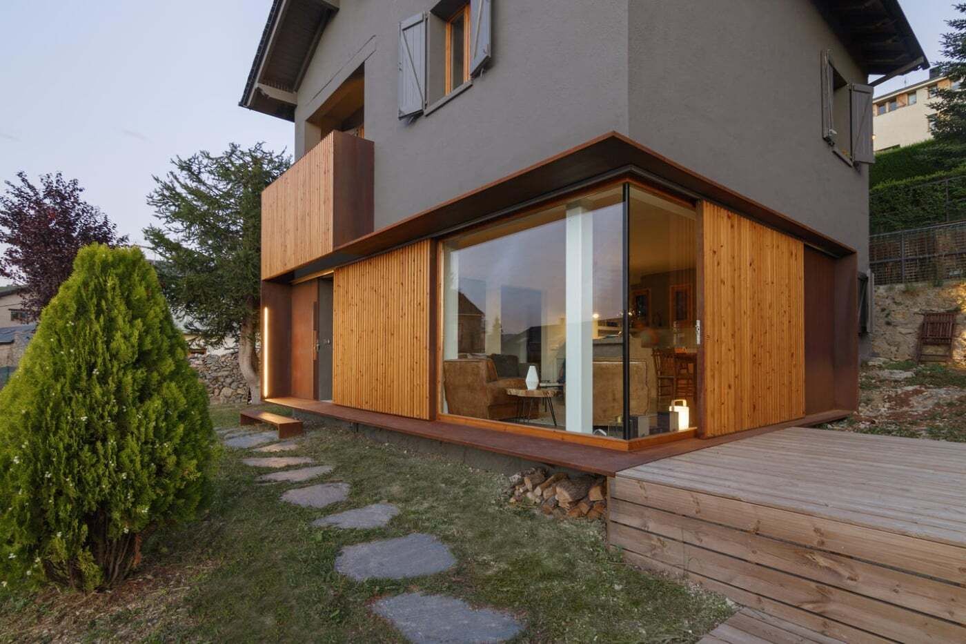 Une maison moderne dotée d’une grande baie vitrée, d’une terrasse en bois et d’un chemin en pierre.