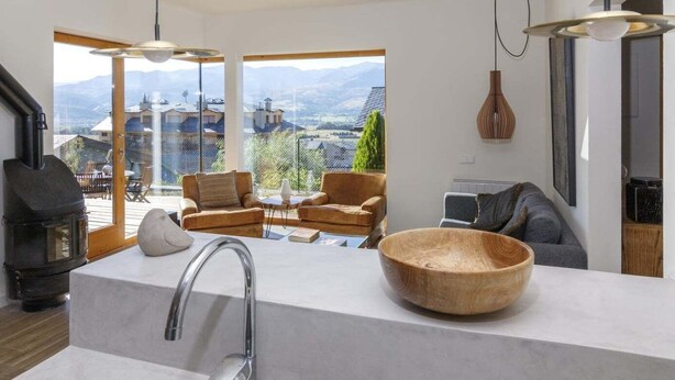 A modern kitchen with a large island, a stone stove, and a view of mountains through large windows.