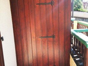 Une porte en bois, dotée d’un loquet métallique et d’un trou de serrure, qui donne sur un balcon avec une rambarde verte.