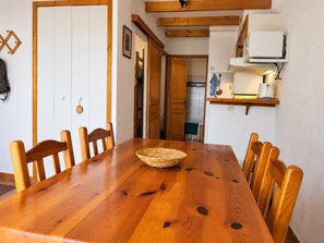 Une table à manger en bois avec des chaises, un panier et un coin cuisine équipé d’un climatiseur.