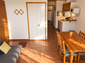 A room with a wooden dining table, chairs, a sofa, and a kitchen area with cabinets and appliances. - Ground Floor 2 rooms Slopeside with Garden and Ski Storage (Bolquère)