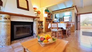 Una sala de estar con chimenea, un comedor con mesa y sillas, y una cocina visible a través de un arco.