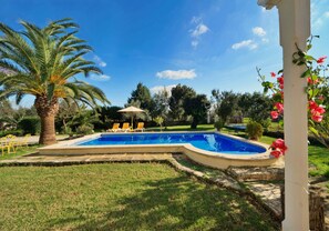Una piscina con una palmera, sillas de descanso amarillas y una pérgola.
