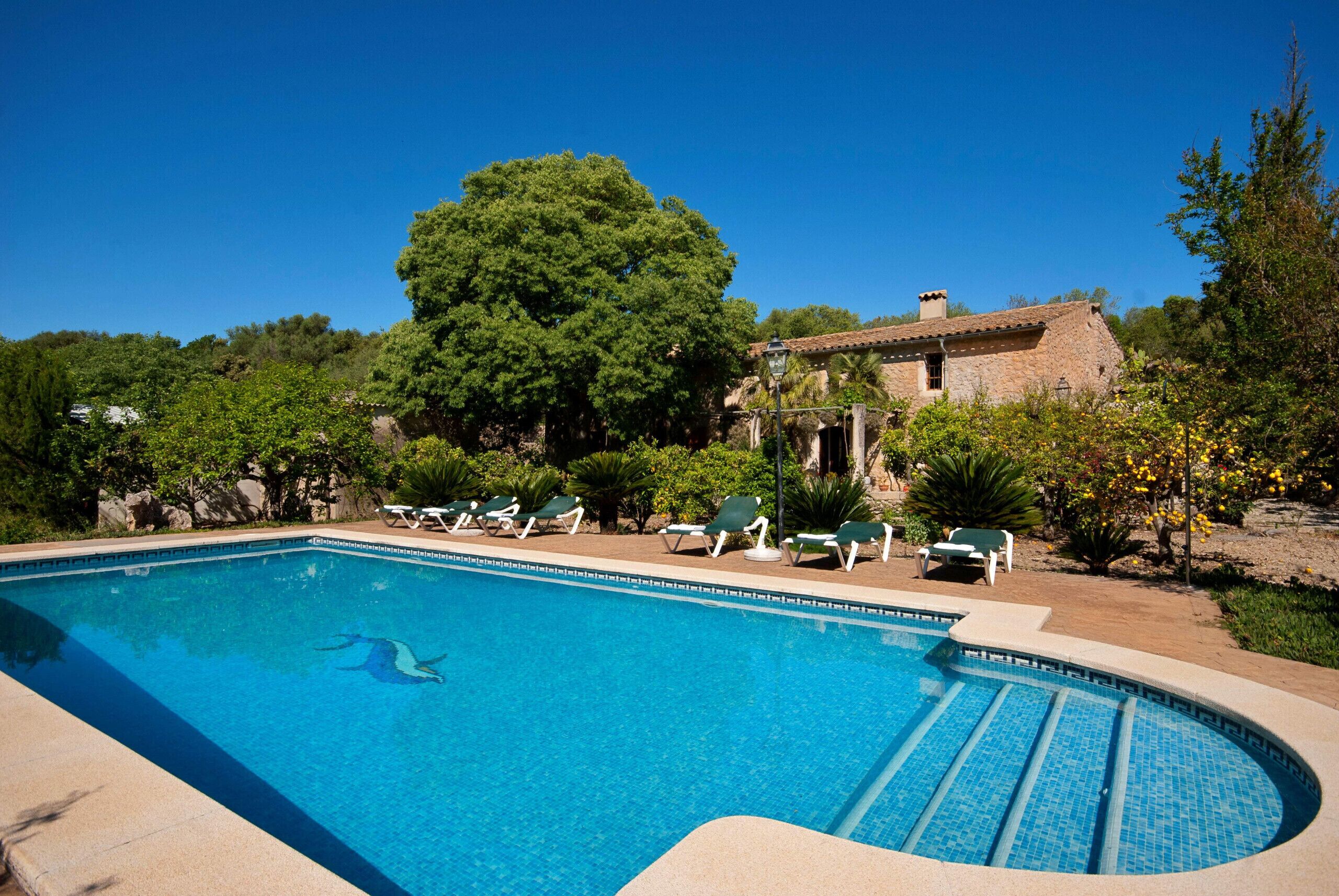 A clear blue swimming pool with lounge chairs and a stone building in the background.