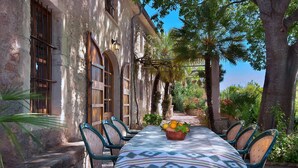 An outdoor dining area with a table set for six, surrounded by stone walls and palm trees. - Hort Den Gelos (Pollensa / Pollença)