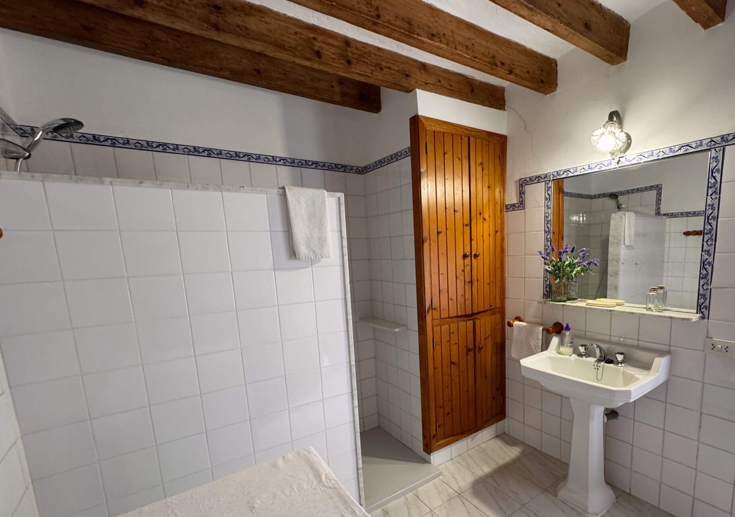 A bathroom with white tiles, a wooden door, a sink with a mirror, and a shower.