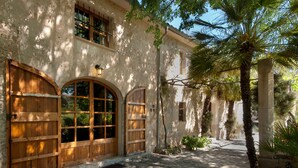 A building with arched wooden doors, a stone facade, and a palm tree. - Hort Den Gelos (Pollensa / Pollença)