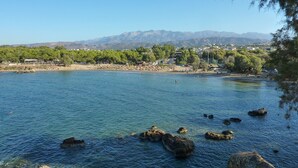 A coastal area with clear water, rocky outcrops, and a distant mountain range. - Maros Spitaki (Varipetro)