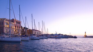 A marina with multiple sailboats docked, buildings with balconies, and a lighthouse in the distance. - Maros Spitaki (Varipetro)
