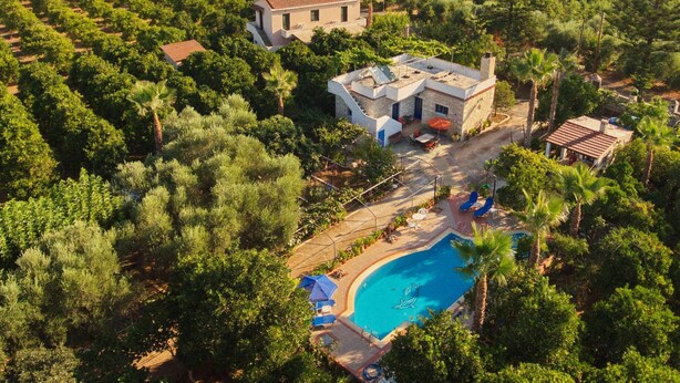 An aerial view of a property with a swimming pool surrounded by lush greenery, a detached house, and a smaller building. - Maros Spitaki (Varipetro)