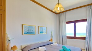A bedroom with a bed, a nightstand, a lamp, a window with a view, and two framed pictures on the wall. - Rouladina Apt 1 (Stalos)
