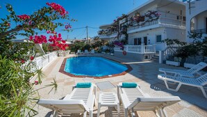 A pool area with white lounge chairs and a clear blue pool surrounded by white buildings with balconies. - Rouladina Apt 1 (Stalos)