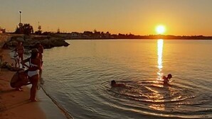 Auringonlasku tyynen vesistön yllä, ja rannalla on ihmisiä.