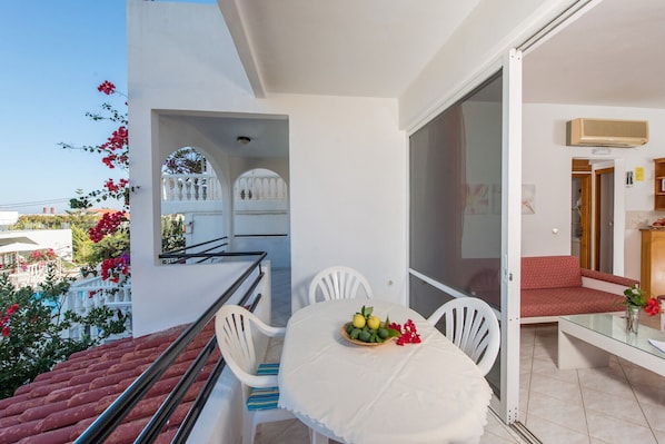 Un balcon avec une table blanche, des chaises et un saladier rempli de fruits.