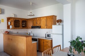 Une cuisine avec des armoires en bois, un îlot central intégré, un four à micro-ondes et un coin repas comprenant une table et des chaises.